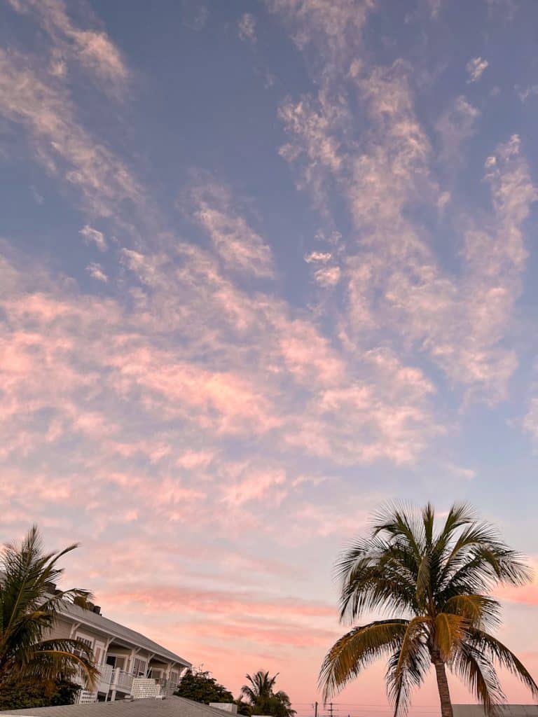 wispy pink clouds in the sky behind a beach house and palm trees
